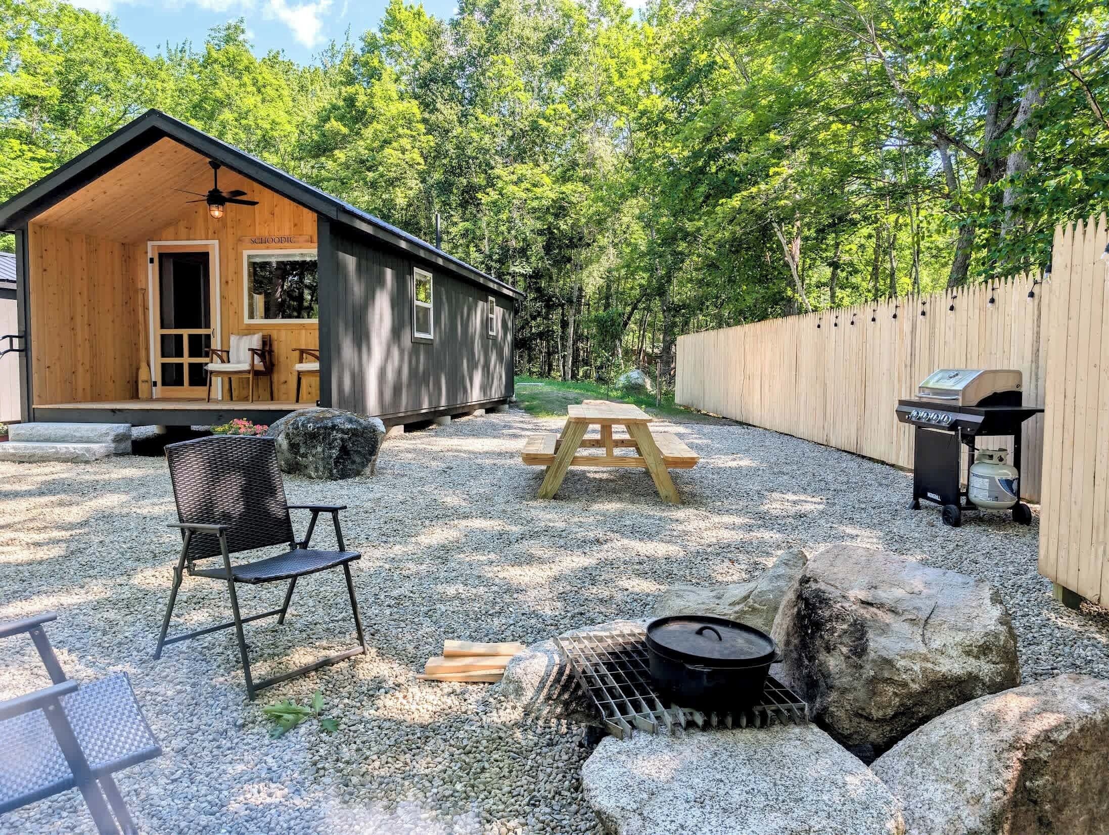 A wooden cabin with a porch, a picnic table, a grill, and a chair.