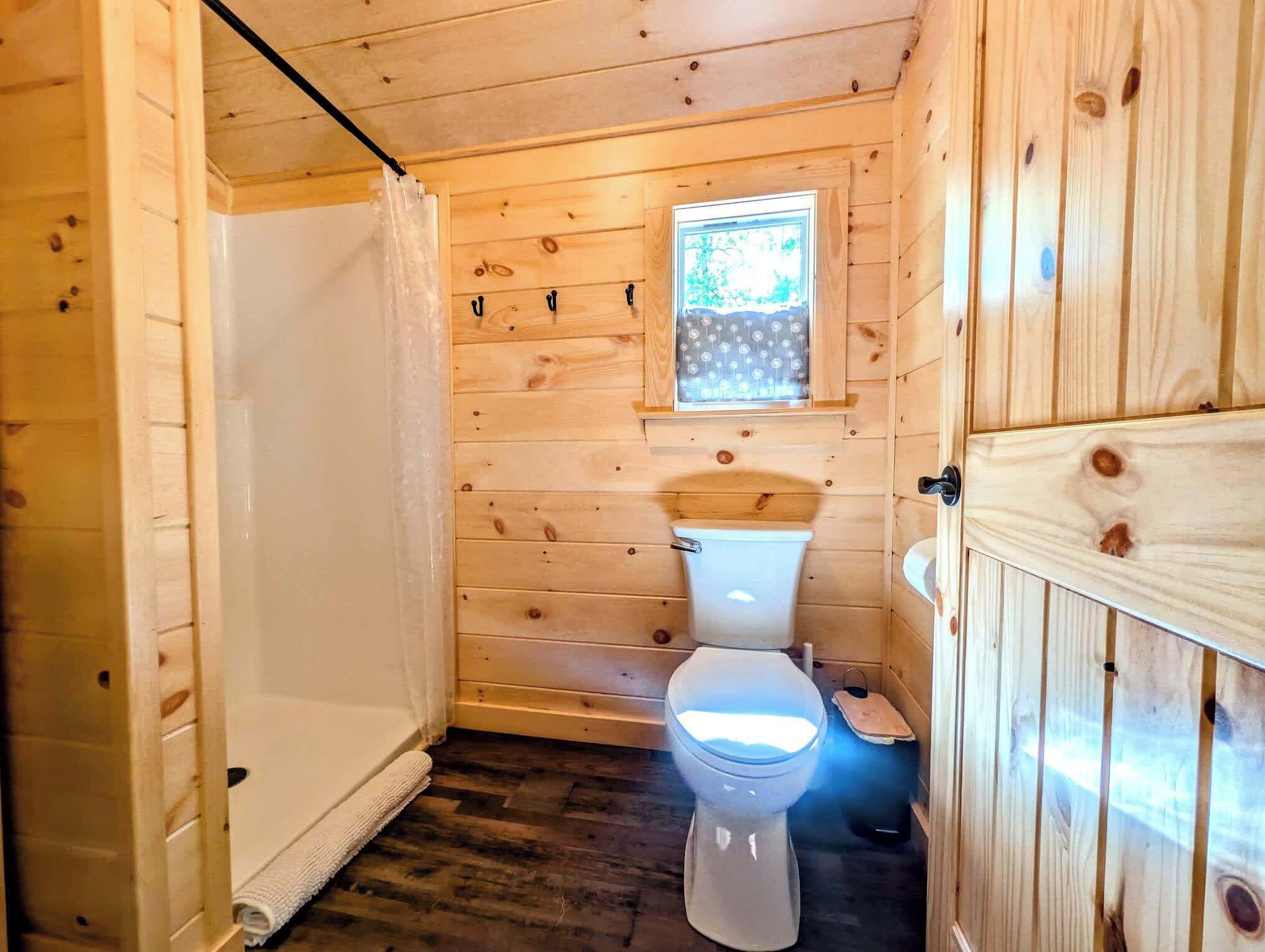 A wooden cabin bathroom with a toilet, a window, and a shower area.