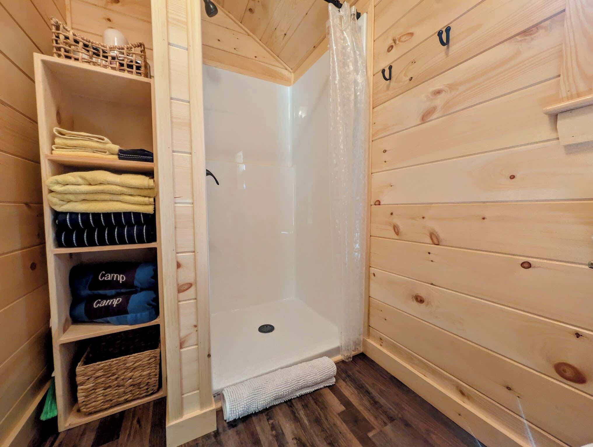 A wooden cabin interior with a shower area, a shelf with folded towels, and a basket.