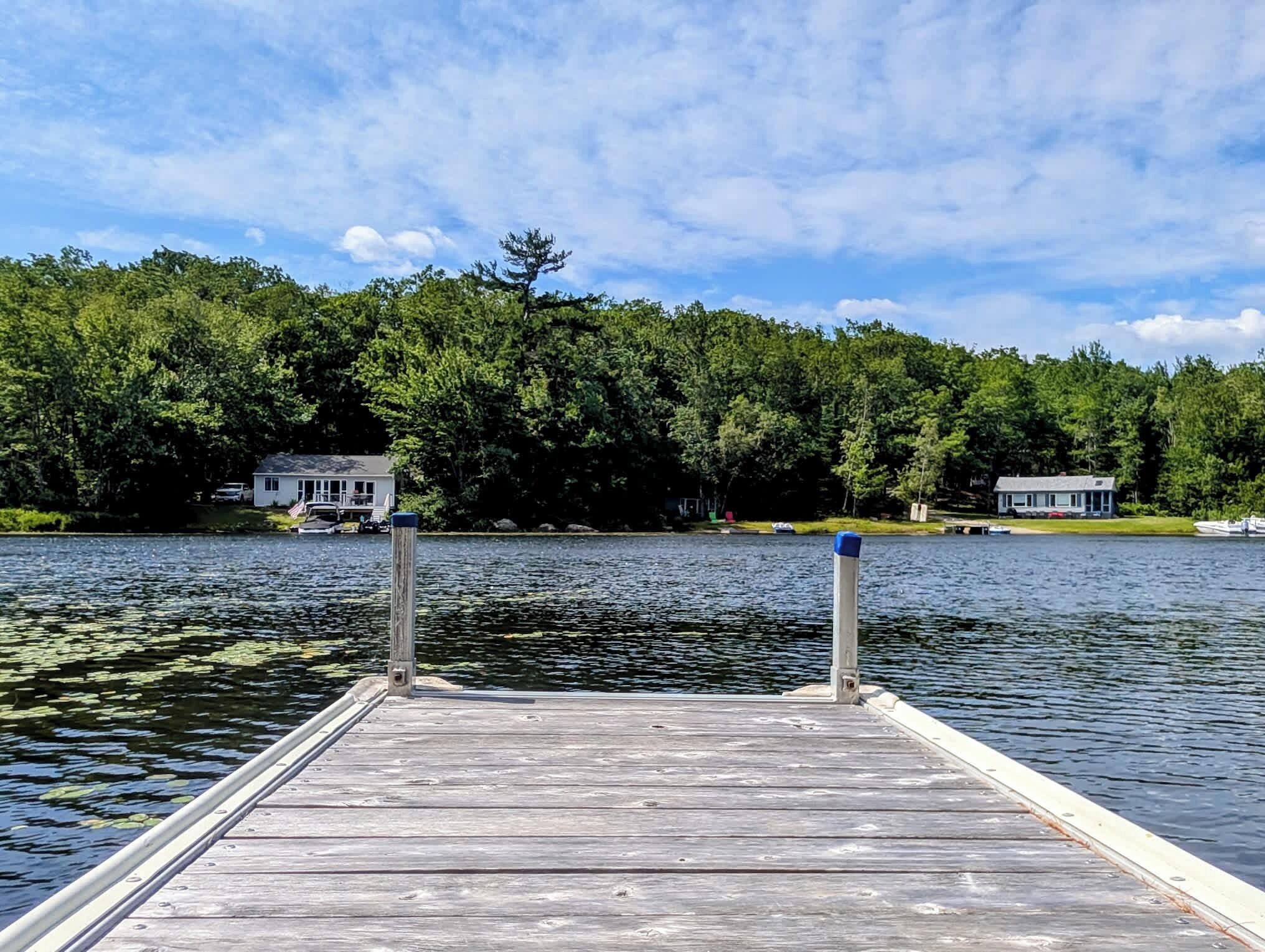 A wooden dock extending into a lake with houses on the opposite shore.