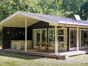 Uma área externa coberta com mesa e cadeiras, grandes janelas e vista para o verde ao redor.