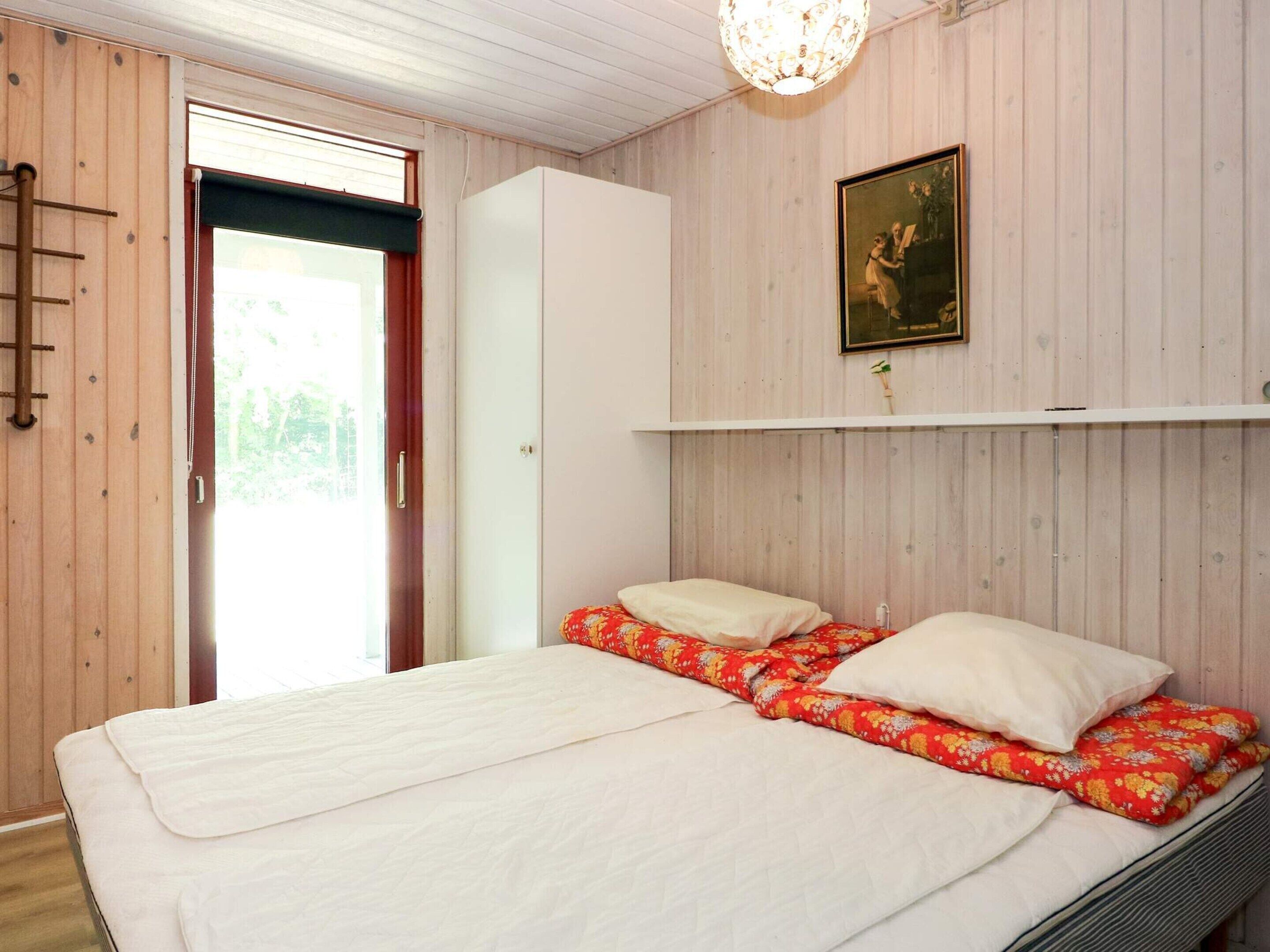 A bedroom with a bed, a wardrobe, a painting, and a window.