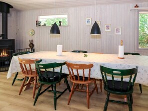 Ein Esszimmer mit einem langen Tisch, vier Stühlen, zwei Pendelleuchten, einem Kamin und gerahmten Bildern an der Wand.