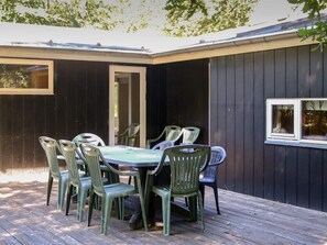 Eine Terrasse im Freien mit Tisch und Stühlen, eine Holzterrasse und ein dunkel gefasstes Gebäude mit einem Fenster.