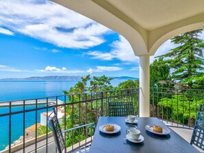 A balcony with a table set for two, overlooking a body of water and greenery. - PALACE PAULINA 3C / HR-10315-03 by Interhome (Novi Vinodolski)