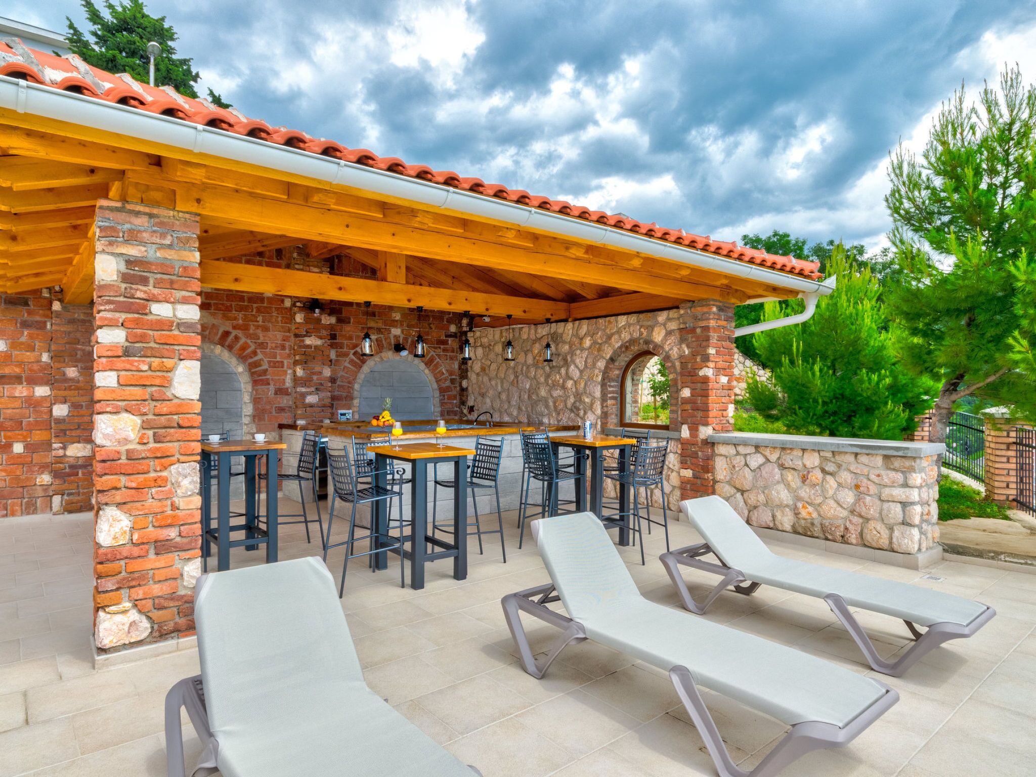 An outdoor patio with stone walls, wooden beams, and a brick fireplace.