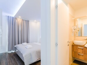 Ein modernes Schlafzimmer mit Bett, Vorhängen und einem Badezimmer mit Waschbecken und Spiegel.