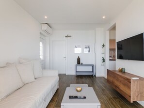 Ein modernes Wohnzimmer mit einem weißen Sofa, einem Couchtisch mit Fernbedienung und einem an der Wand befestigten Fernseher.