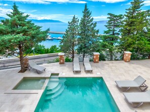 A swimming pool with lounge chairs, a view of the sea, and trees. - PALACE PAULINA 3C / HR-10315-03 by Interhome (Novi Vinodolski)