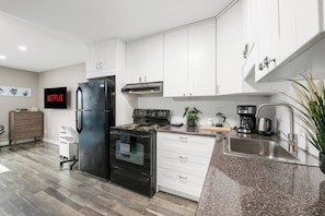 Eine moderne Küche mit weißen Schränken, einem schwarzen Kühlschrank, einem Herd und einer Kaffeemaschine.