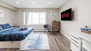 Een moderne slaapkamer met een bed, een bureau, een stoel, een televisie en een raam.