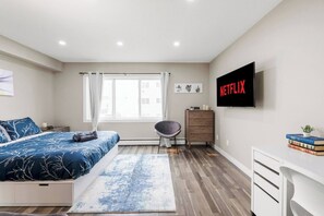 Ein modernes Schlafzimmer mit Bett, Schreibtisch, Stuhl, Fernseher und Fenster.