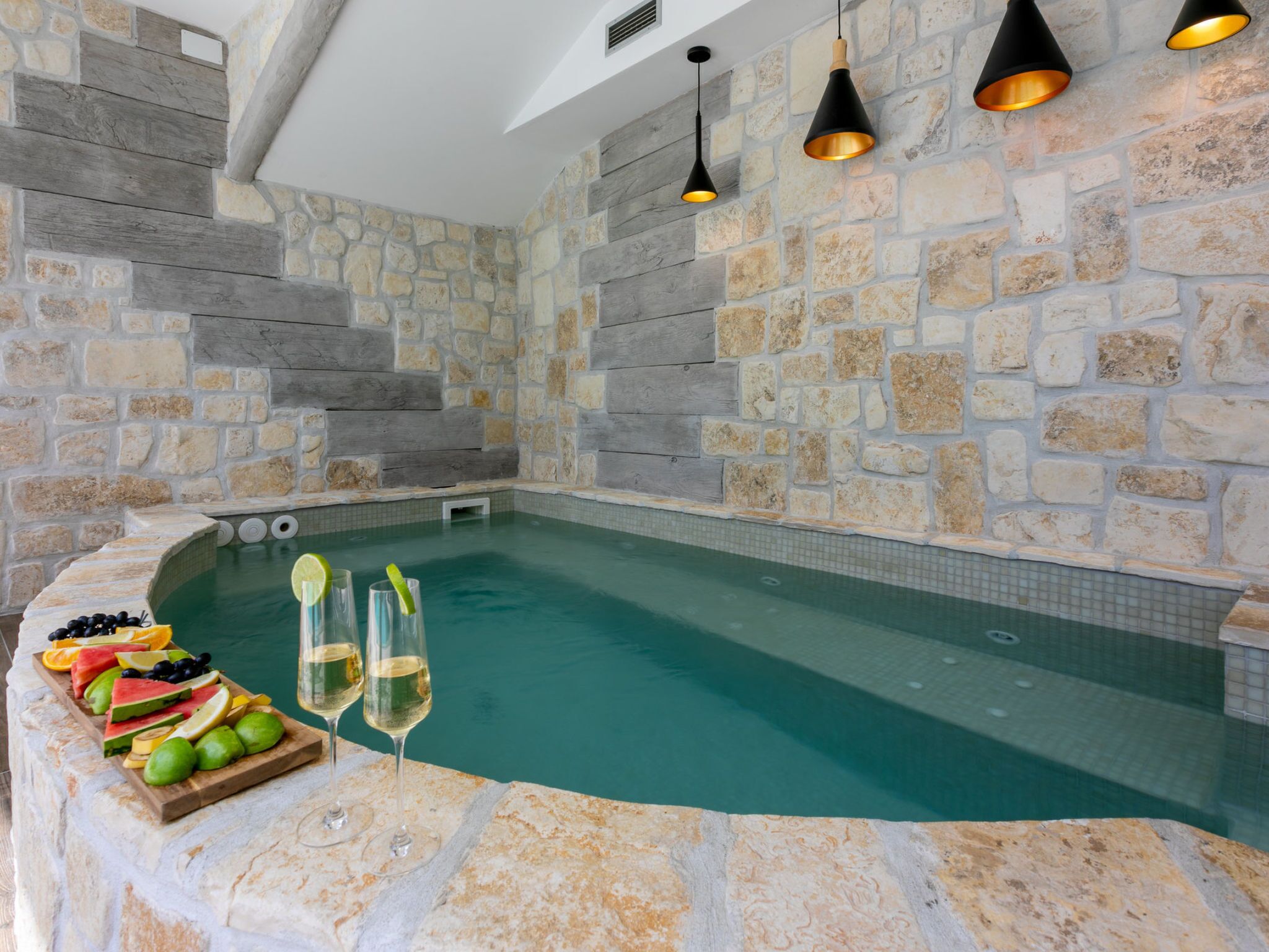 A stone-walled indoor pool with a seating area and glasses of wine.