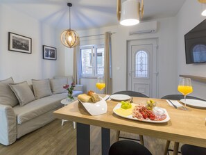 A modern living room with a sofa, a dining table set with food, and a large window with curtains. - PALACE PAULINA 2B / HR-10322-01 by Interhome (Novi Vinodolski)
