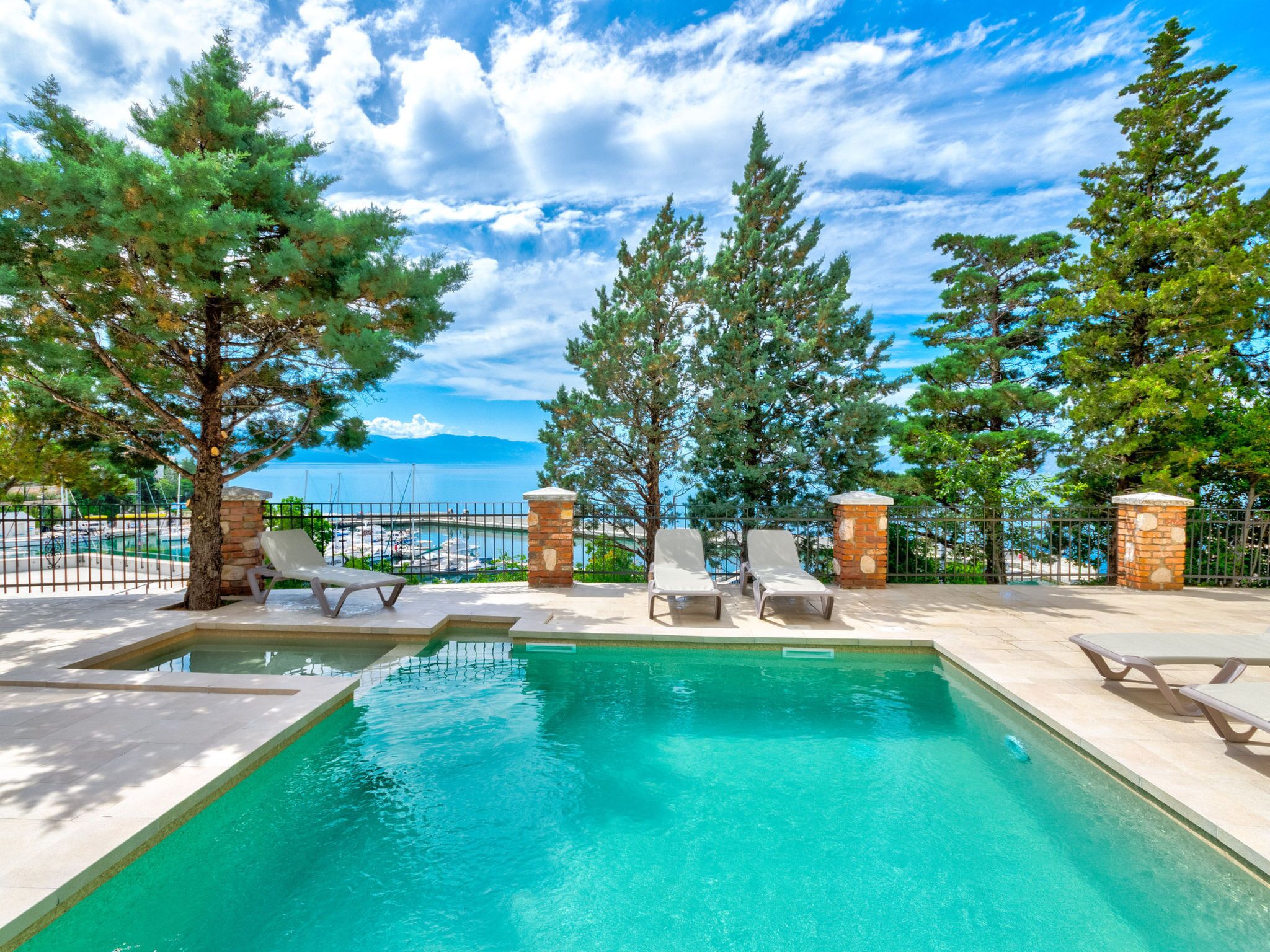 A swimming pool with lounge chairs, surrounded by trees and a view of the sea.