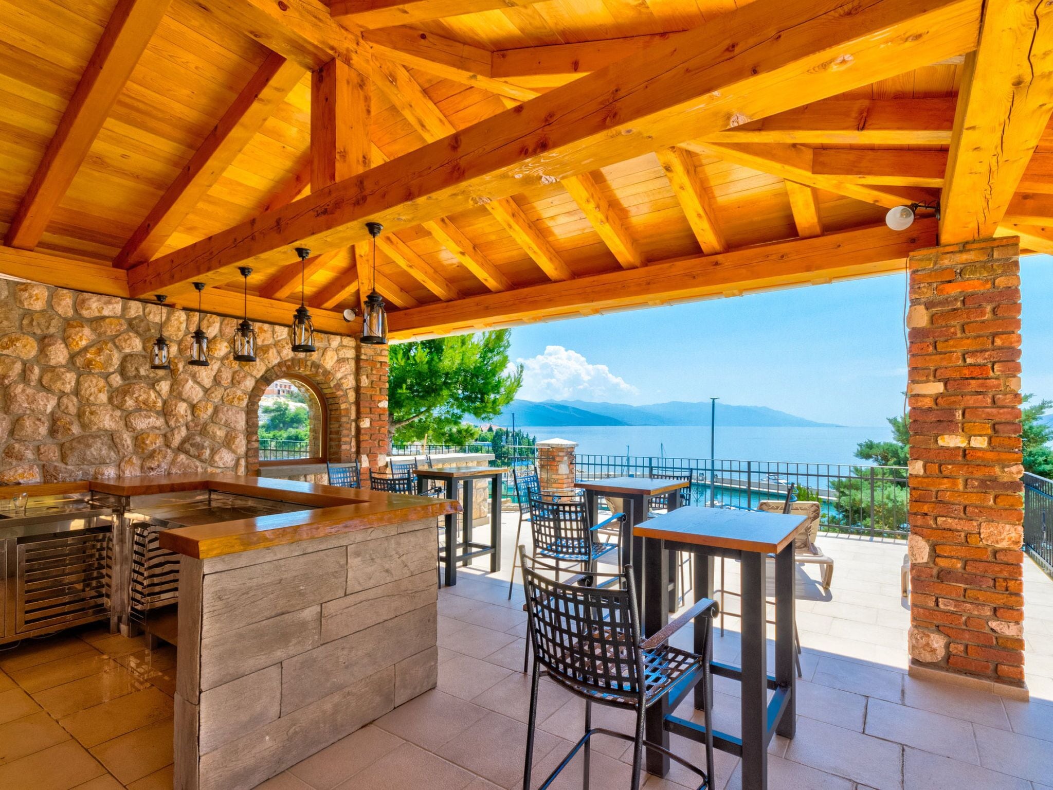 Eine Terrasse im Freien mit einer Steinwand, einer Holzbalkendecke und Blick auf das Meer.