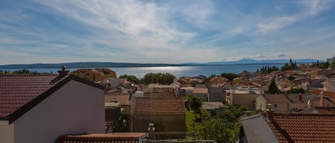 A coastal town with terracotta-roofed buildings, a clear sky, and a body of water in the distance.