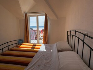 Quarto com uma cama, janela com cortinas e vista para um corrimão vermelho lá fora.