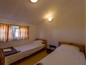 Ein Zimmer mit zwei Einzelbetten, einem Fenster mit Vorhängen, einem Nachttisch mit Lampe sowie einer Wandleuchte.