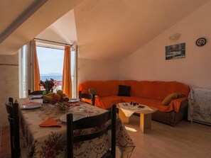 Ein Essbereich mit Tisch für zwei Personen, einer Couch und einem kleinen Tisch mit Laptop und Kopfhörern.