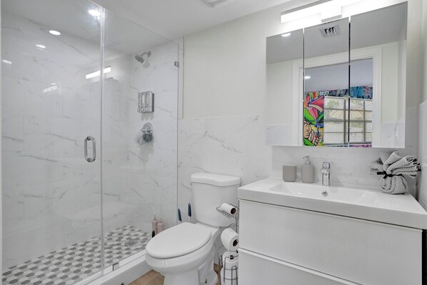 A modern bathroom with a glass-enclosed shower, a toilet, and a sink with a mirror above. - MiamiMuralHouse:4BRw/Themes, Gameroom, Backyard (Miami)