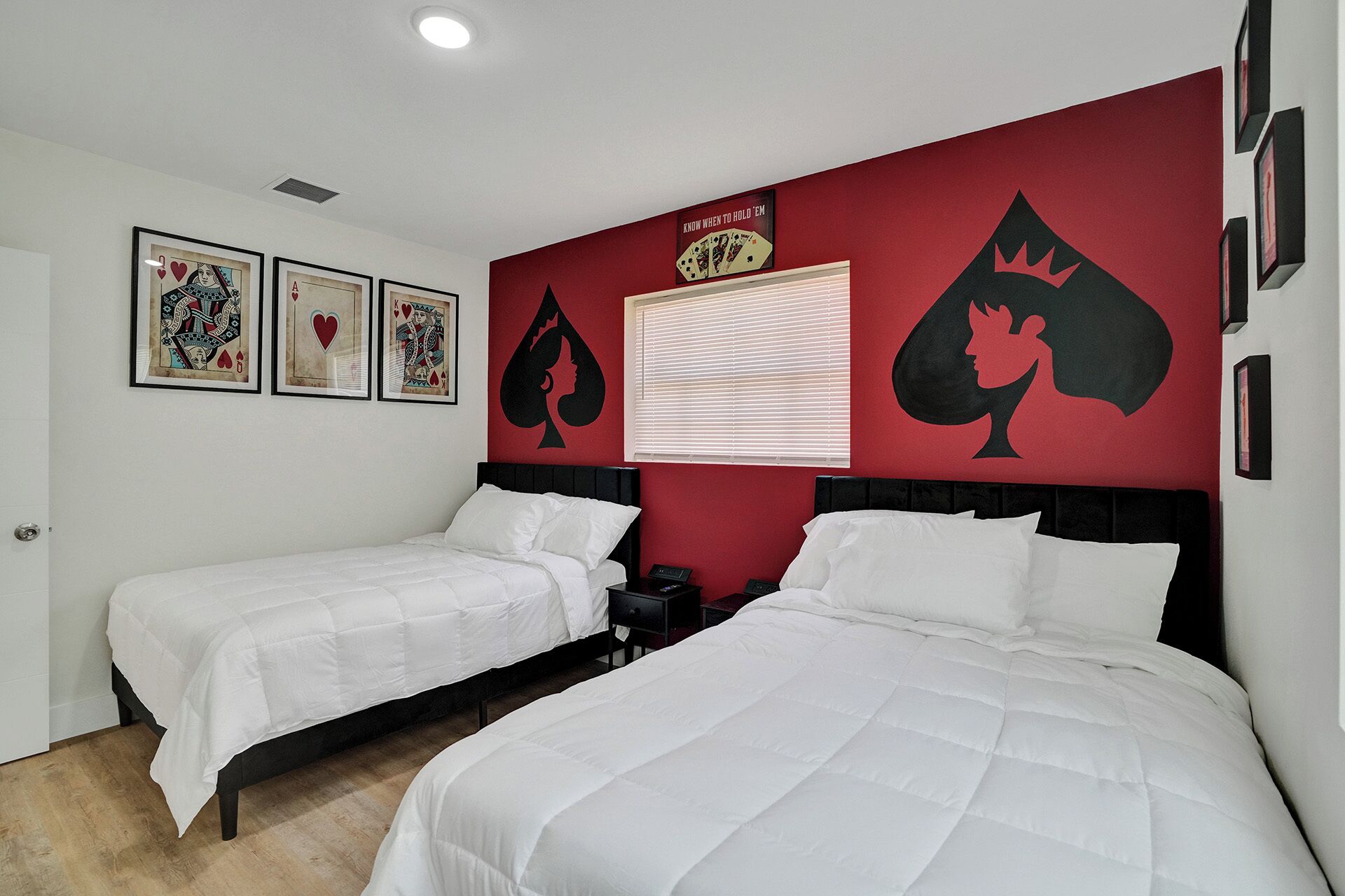 Habitación de hotel con dos camas, una pared de acento roja y decoración temática de cartas de juego.