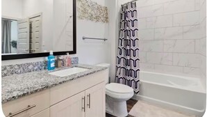 Un bagno con il water bianco, un lavabo con specchio, una doccia con tenda decorata e una parete piastrellata.