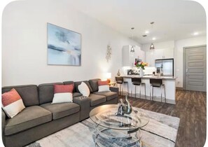 A living room with a grey sofa, a glass coffee table, and a kitchen area in the background. - Modern & Lavish luxury 1 bedroom/1 bath in Deep Ellum Downtown Dallas (Dallas)
