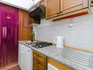 A kitchen with wooden cabinets, a gas stove, a white kettle, and a tiled backsplash. - GOLIC Wine / HR-03619-03 by Interhome (Crikvenica/Dramalj)