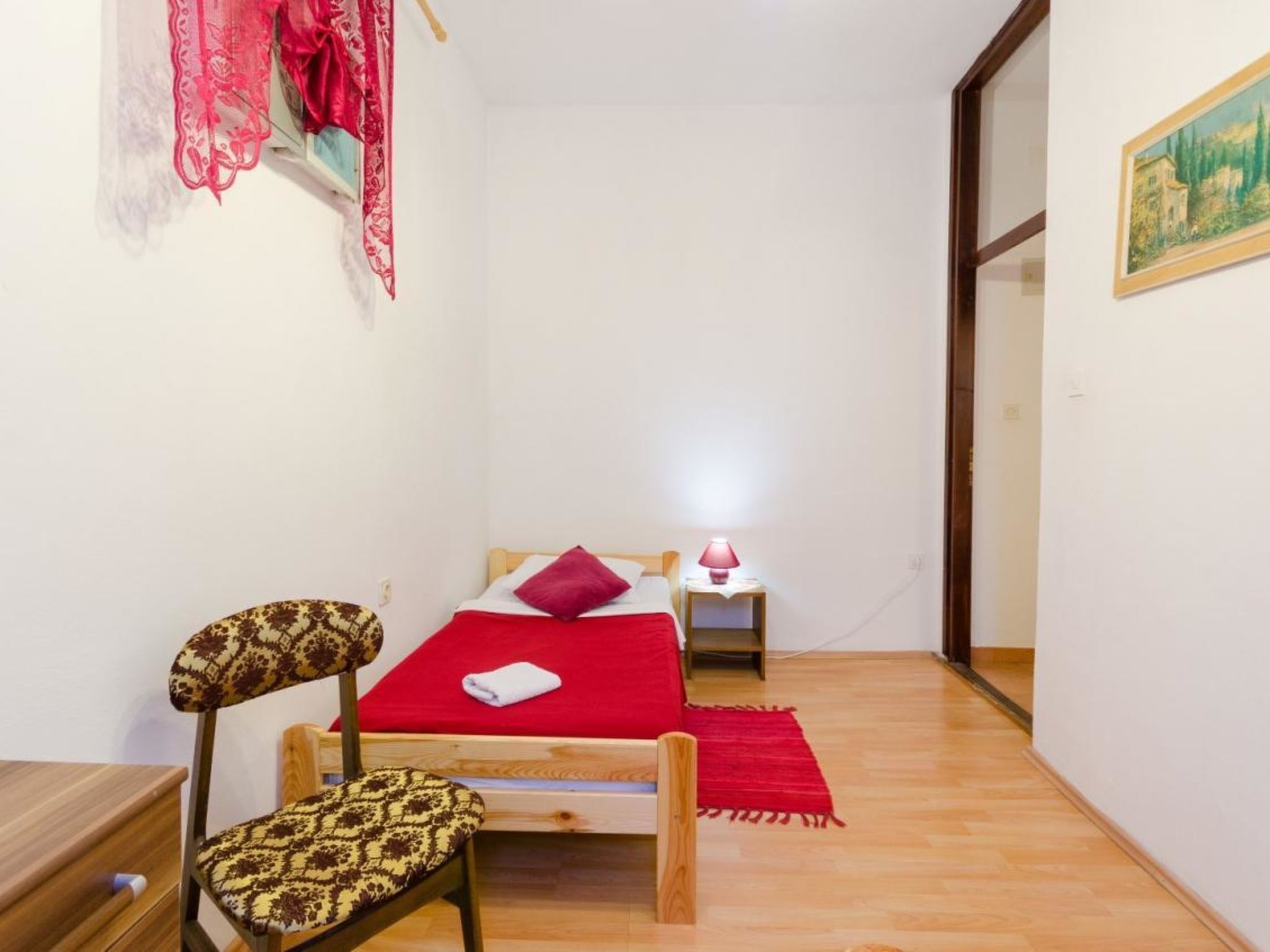 A small room with a bed, a chair, a nightstand, and a lamp.