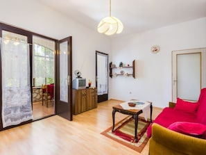 A room with a wooden floor, a red sofa, a table with a rug, a television on a cabinet, and a sliding glass door leading to an outdoor area. - GOLIC Wine / HR-03619-03 by Interhome (Crikvenica/Dramalj)