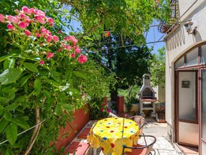 Une terrasse avec une table et des chaises, entourée de verdure et agrémentée d’un barbecue.