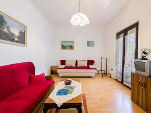 Un salon avec un canapé rouge, un canapé blanc avec des coussins rouges, une table basse en bois ornée d’un objet décoratif et un téléviseur posé sur un meuble en bois.