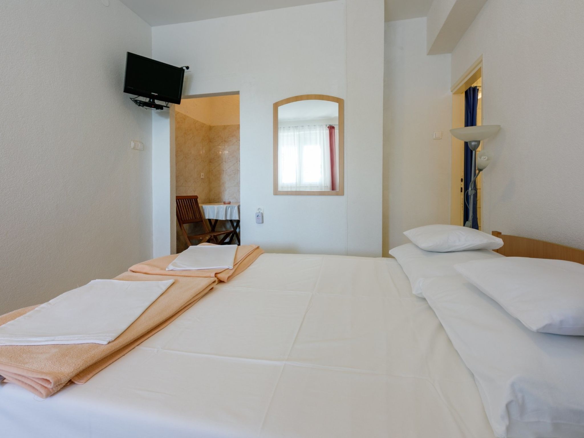 A hotel room with a bed, a television mounted on the wall, a mirror, and a lamp.