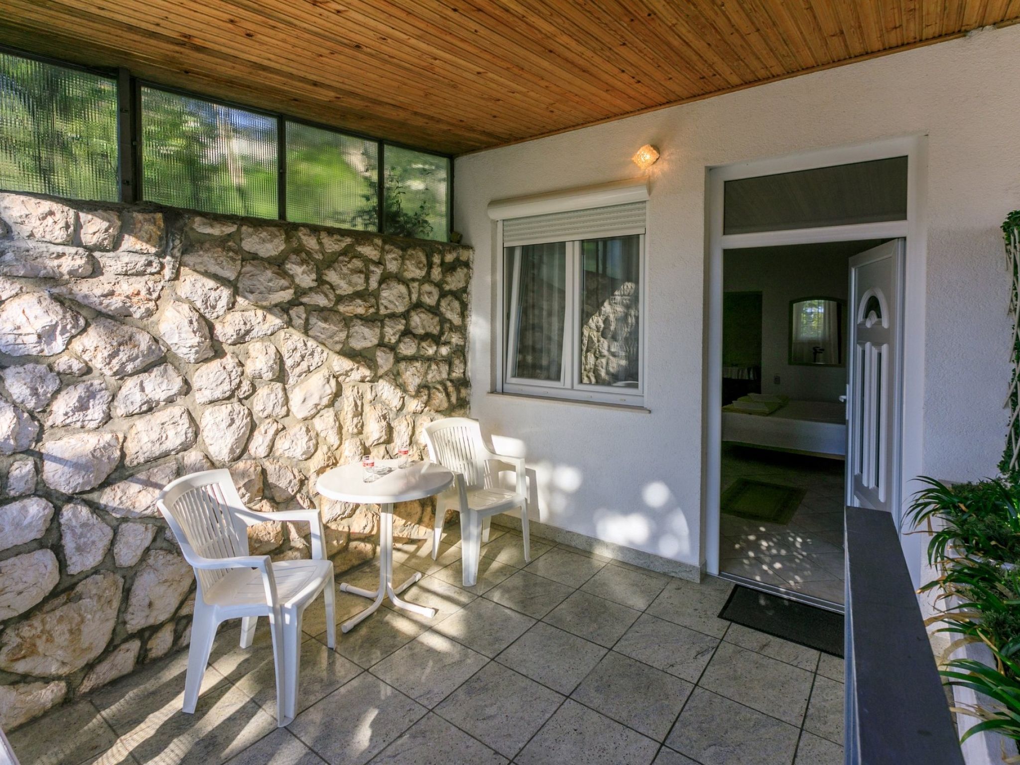 A stone wall, a wooden ceiling, a window, a door, and a small table with chairs.