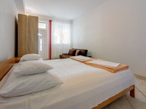 Une chambre d’hôtel comprenant un lit, des oreillers, une table de chevet, une chaise, un panneau en bois et une fenêtre avec des rideaux.