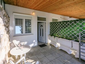 Eine überdachte Terrasse mit einer Steinwand, einer weißen Tür, einem weißen Tisch mit Stühlen und einer dekorativen Gitterwand.