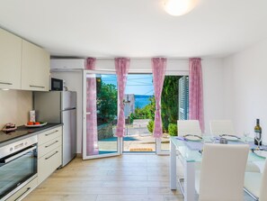 Ett modernt kök med matplats, utsikt över havet och en uteplats med rosa gardiner.