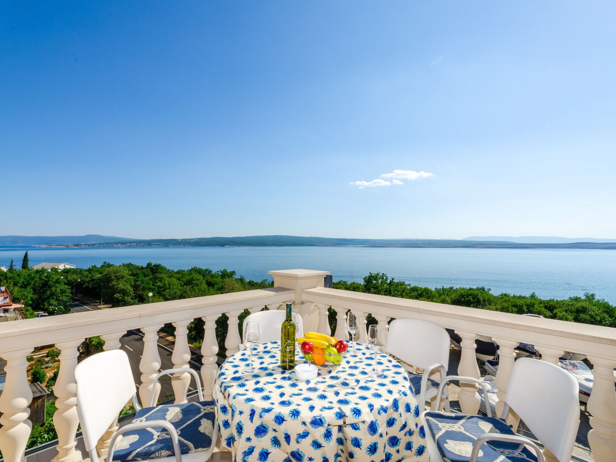 A terrace with a table set for dining, overlooking a body of water and distant land.
