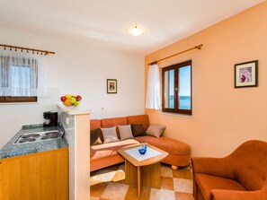 Un espacio habitable compacto con kitchenette, un sofá, una mesita y vista al mar.