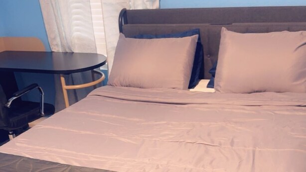 Uma cama com cabeceira acolchoada escura, uma mesinha de cabeceira e uma cadeira.