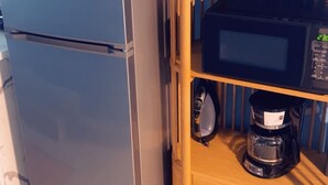 Uma cozinha compacta com geladeira de aço inoxidável, micro-ondas e cafeteira, tudo sobre uma prateleira de madeira.