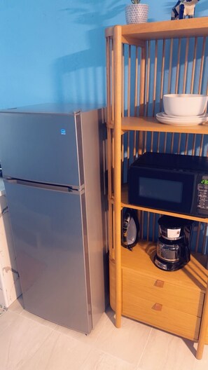 A compact kitchen with a stainless steel refrigerator, a microwave, and a coffee maker on a wooden shelf. - Cozy 1-bedroom studio in perfect Lauderdale Lakes with AC & Pool access (Lauderdale Lakes)