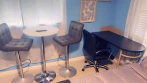 Um quarto com uma mesa redonda, dois bancos altos, uma cadeira de escritório preta e uma cama.