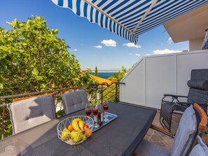 Ein Balkon mit Tisch, Stühlen, einer Obstschale und einem Tablett mit Gläsern und Flaschen.