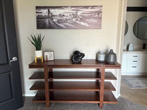 A wooden desk with shelves, a cityscape painting, a cactus, a framed sign, and decorative vases. - Desert Oasis on Washinton St (Avondale)