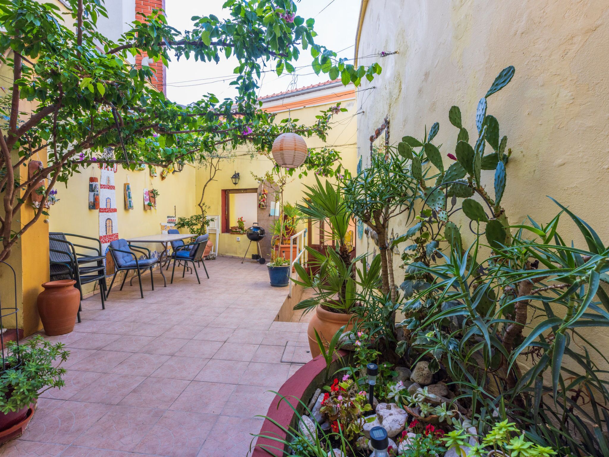 Une terrasse extérieure avec des chaises et des tables, entourée de plantes en pot et d’un petit jardin.