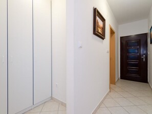 A hallway with white walls, a tiled floor, a wooden door, and a framed picture on the wall. - Omega Cert / HR-09851-01 by Interhome (Crikvenica)