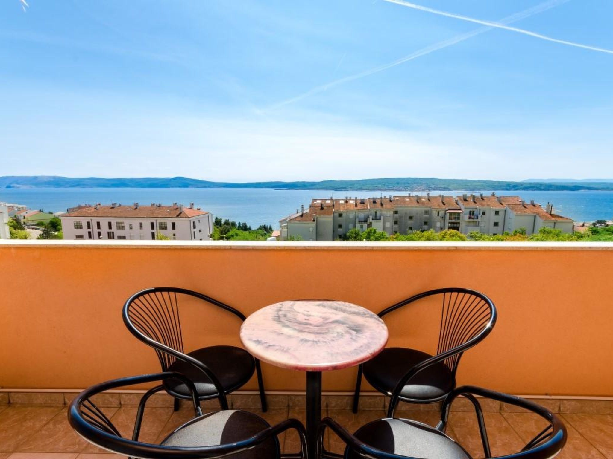 Eine Terrasse mit zwei Stühlen und einem Tisch, mit Blick auf ein Gewässer und Gebäude.