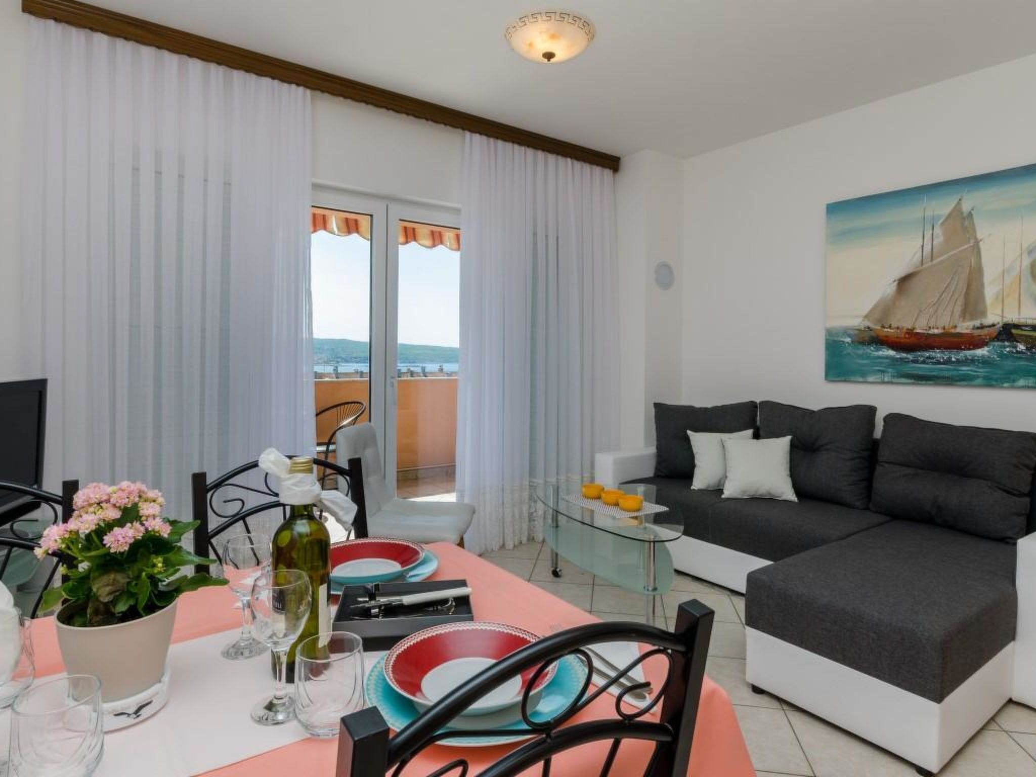 A modern living room with a sofa, a dining table set for two, and a balcony with curtains.